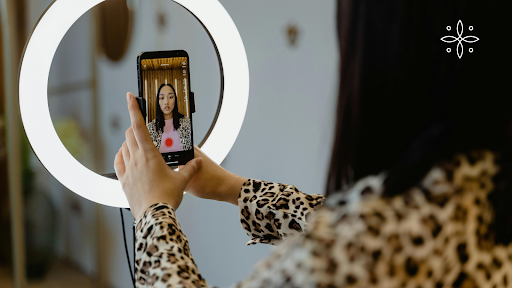 A woman records a video on her smartphone with a ring light.